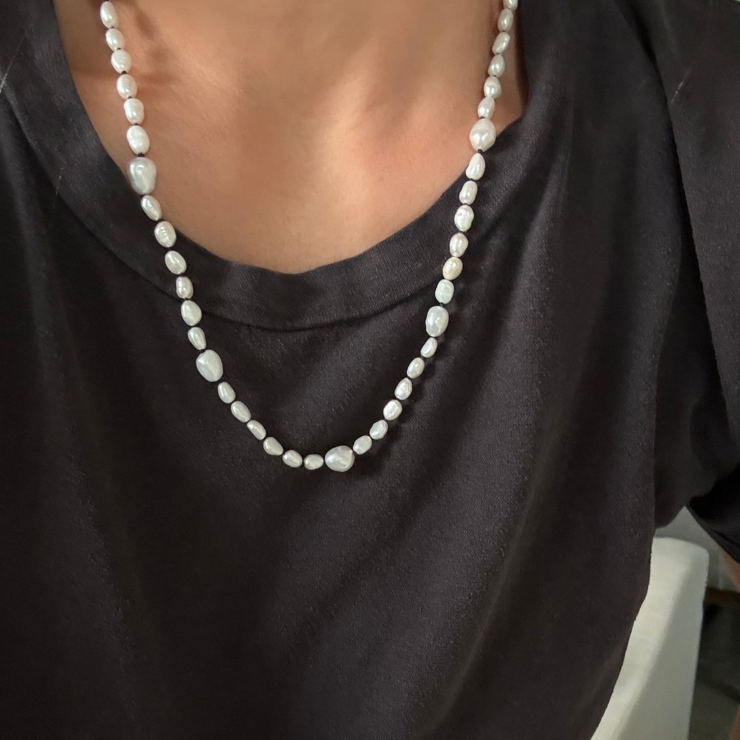 A close-up of a person wearing a double-strand pearl necklace over a dark charcoal gray t-shirt.