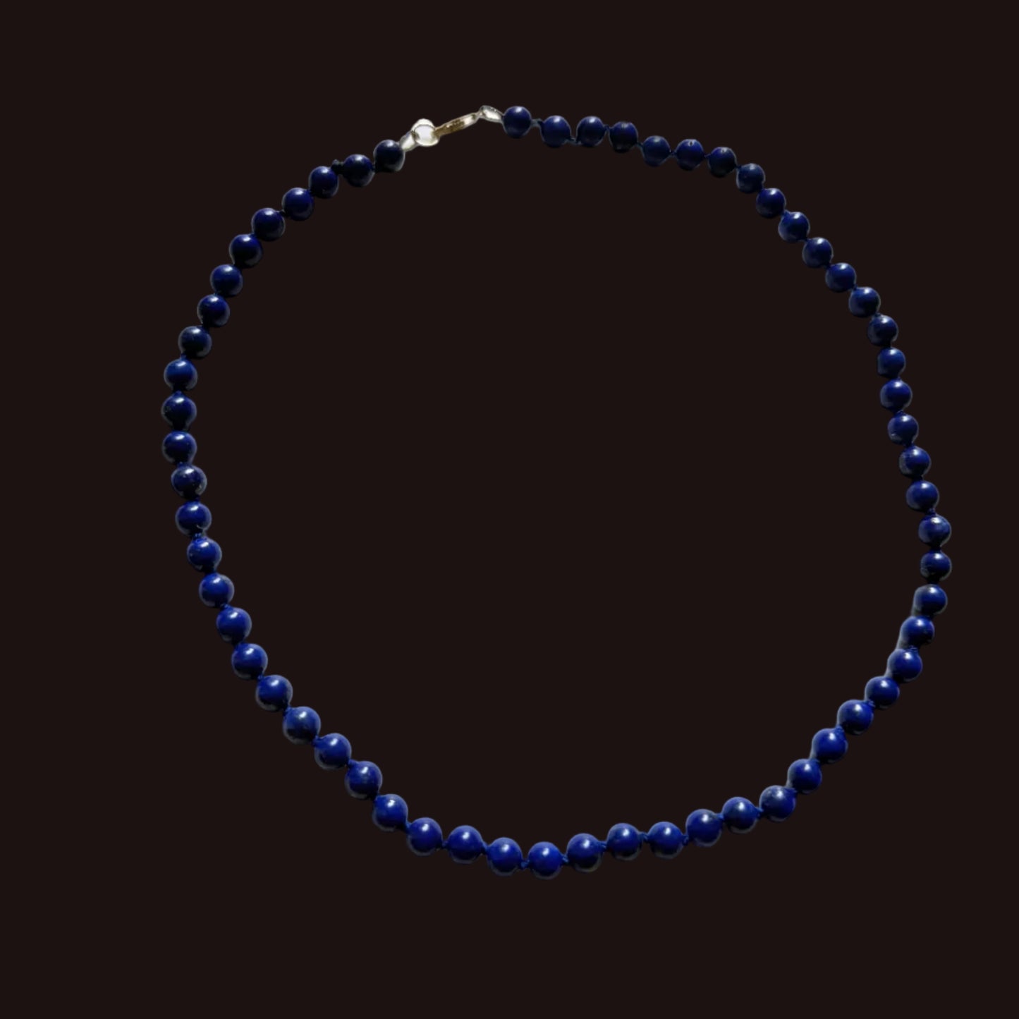 A beaded necklace made of small dark blue lapis lazuli-style beads with a gold clasp, laid flat on a white surface.