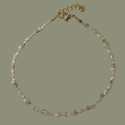 Beaded anklet with gold clasp on a plain background