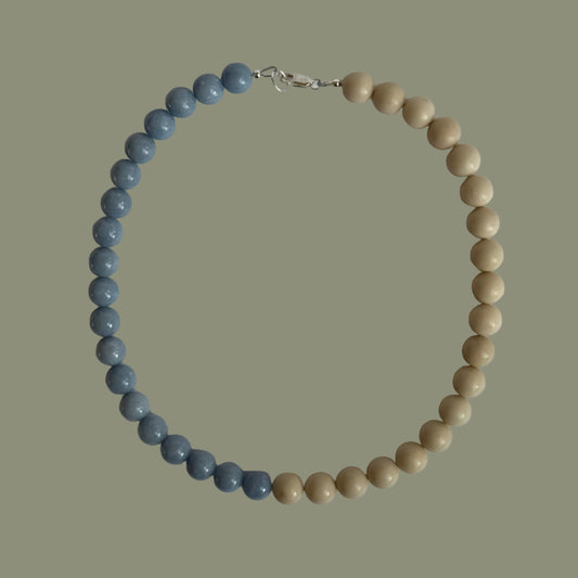 Beaded necklace with blue and beige beads on a light gray background