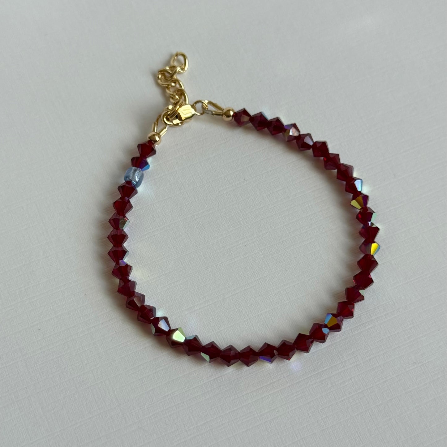Bracelet with red beads and gold clasp on a light gray background