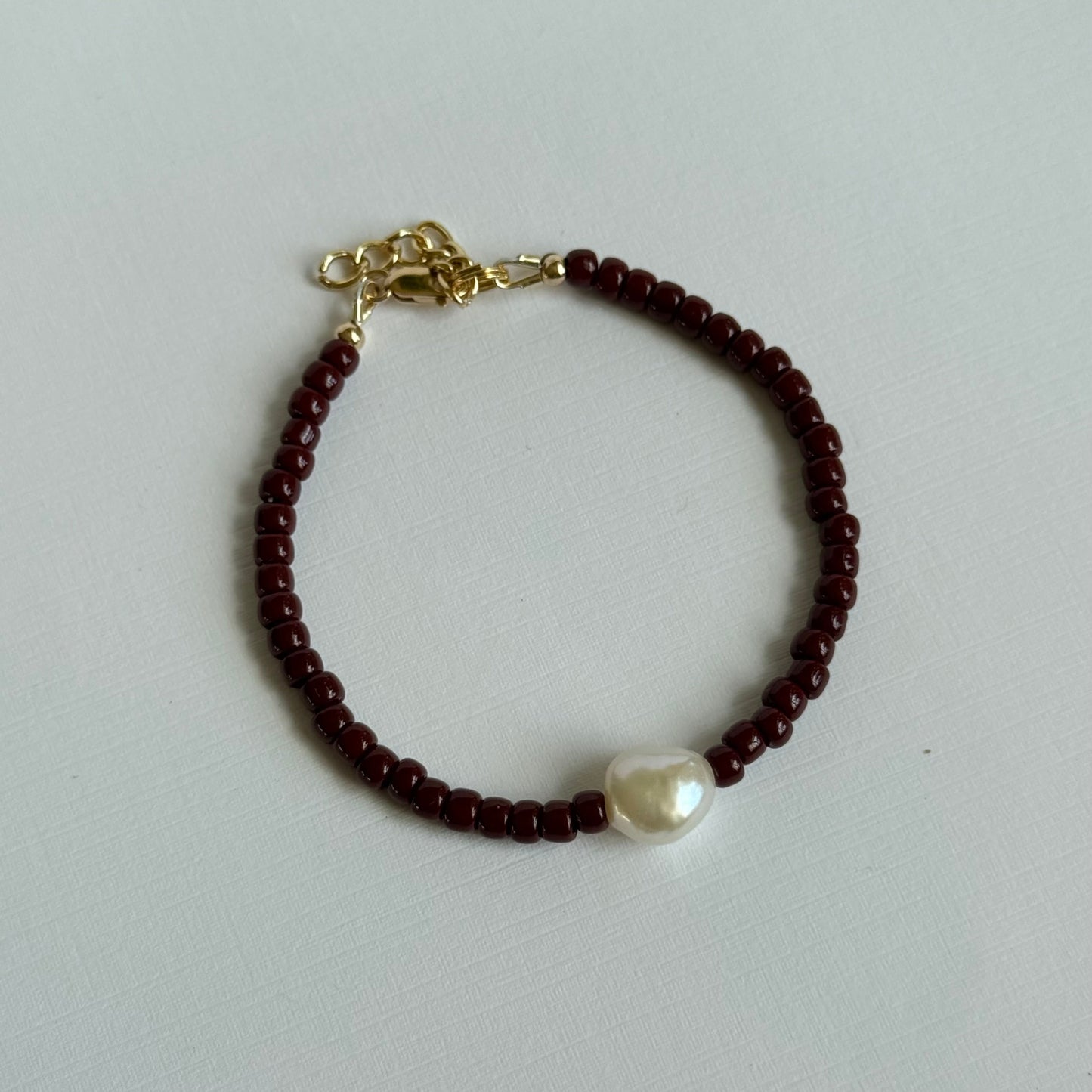 Bracelet with red beads and a pearl on a light gray background