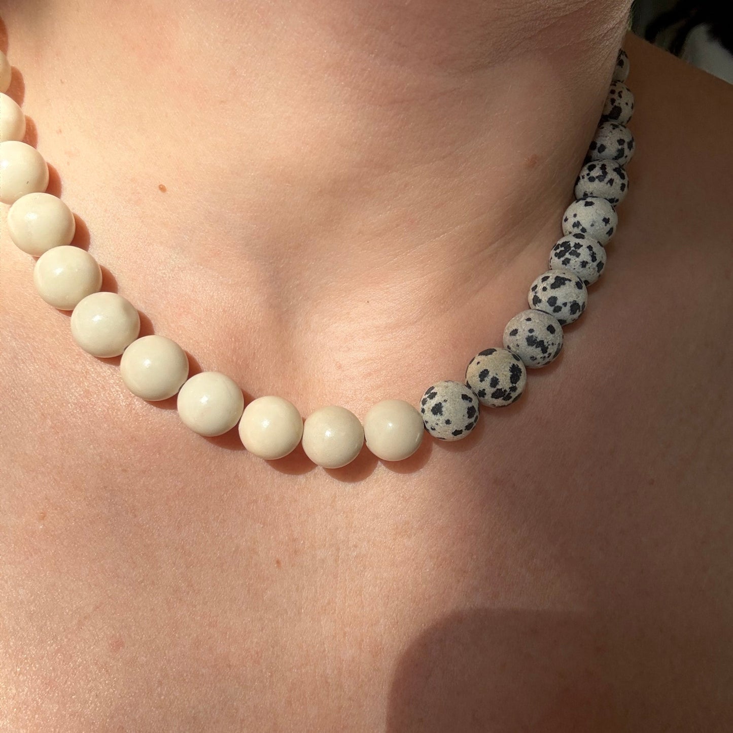 Close-up of a white beaded bracelet with black spots on a person's wrist.