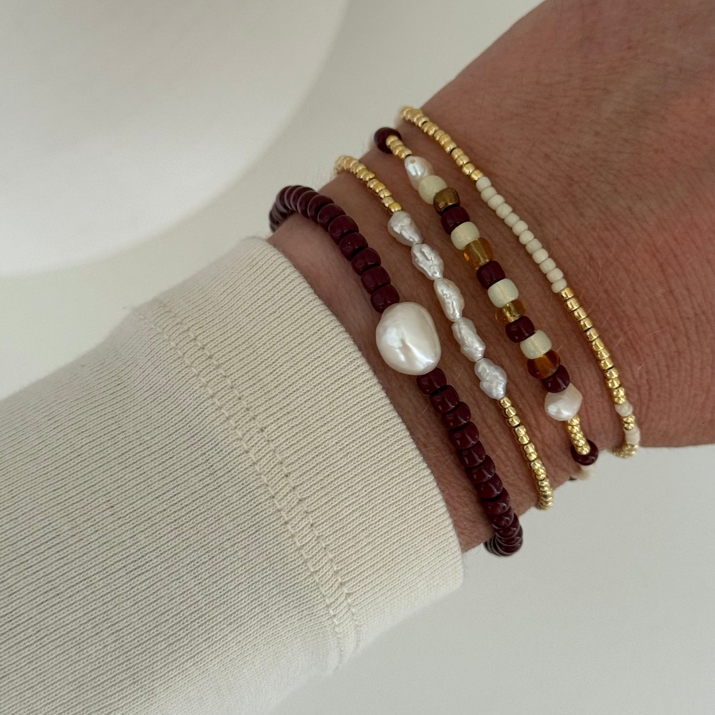Close-up of a wrist wearing multiple beaded bracelets on a neutral background