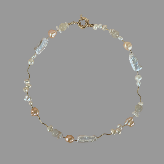 A necklace with a variety of freshwater pearls in different shades of white and peach, interspersed with gold filled tube beads, on a gold filled closure.