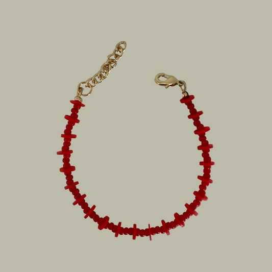 A red beaded bracelet with gold filled closure, laid out on a flat surface.