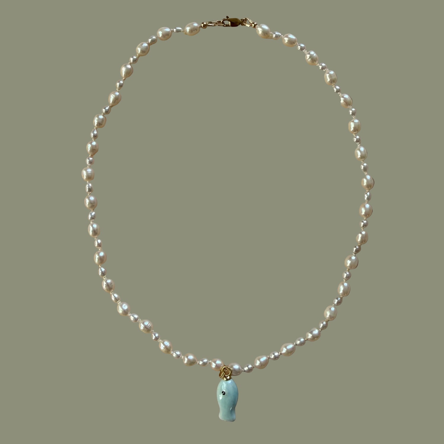 Pearl necklace with a small green pendant on a beige background
