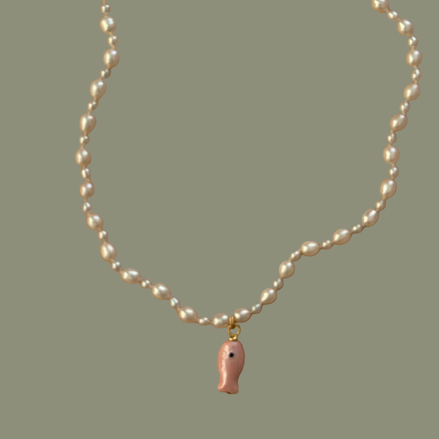 Pearl necklace with a small pink fish charm on a beige background