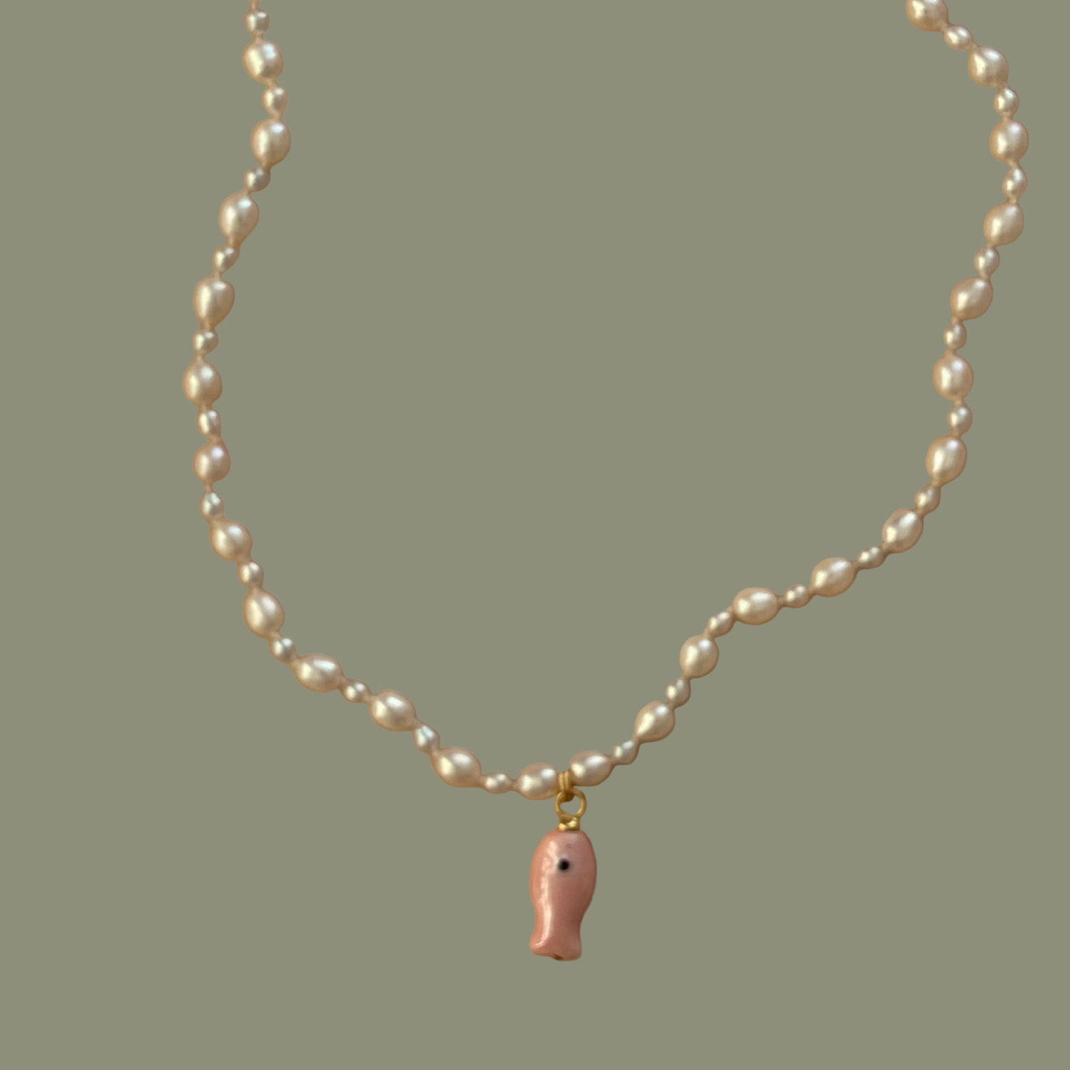 Pearl necklace with a small pink fish charm on a beige background