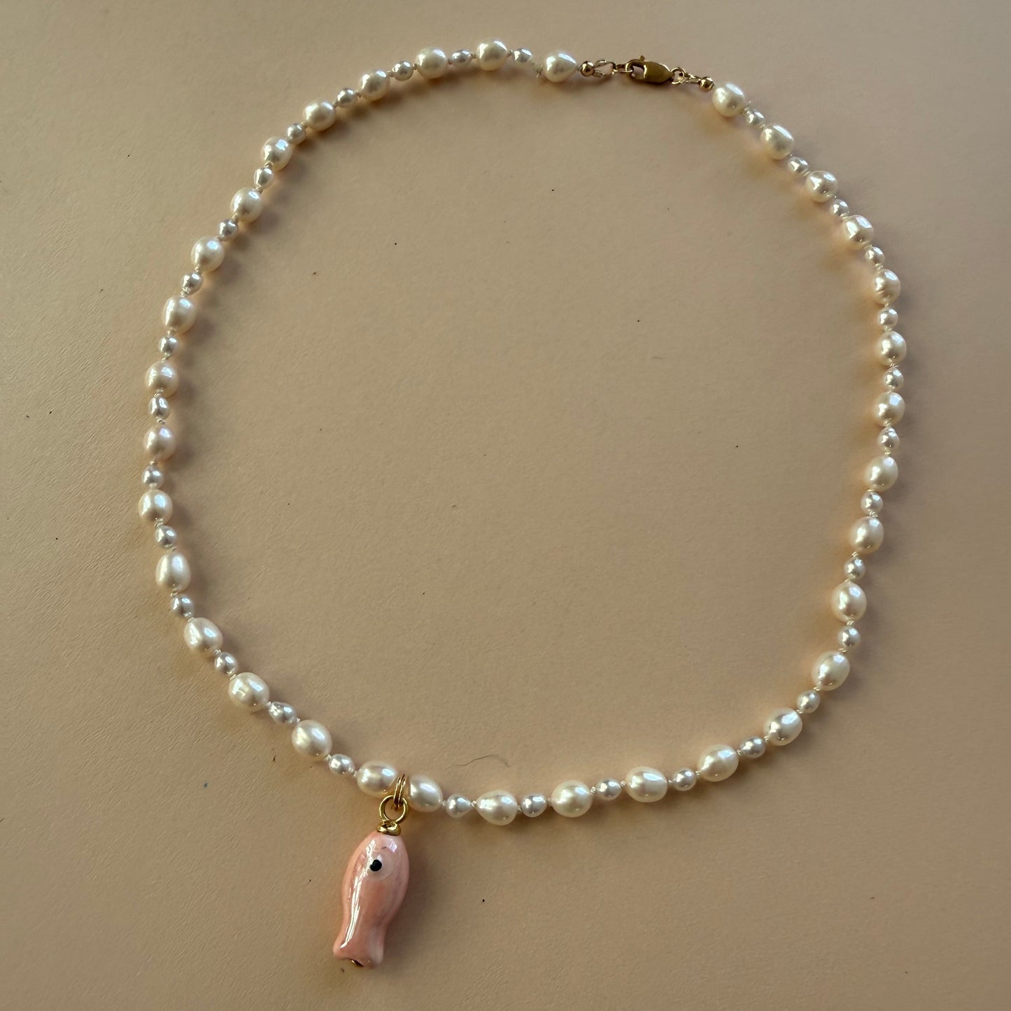 Pearl necklace with a small fish charm on a beige background