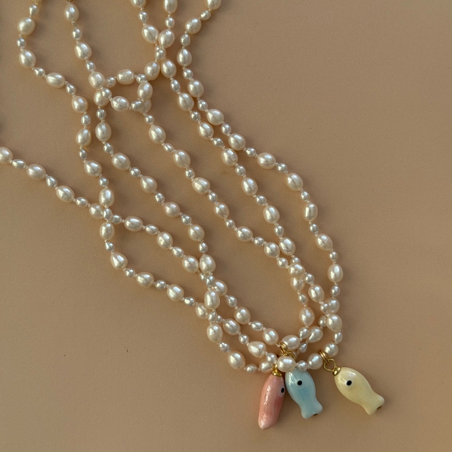 Pearl necklace with fish-shaped charms on a beige background