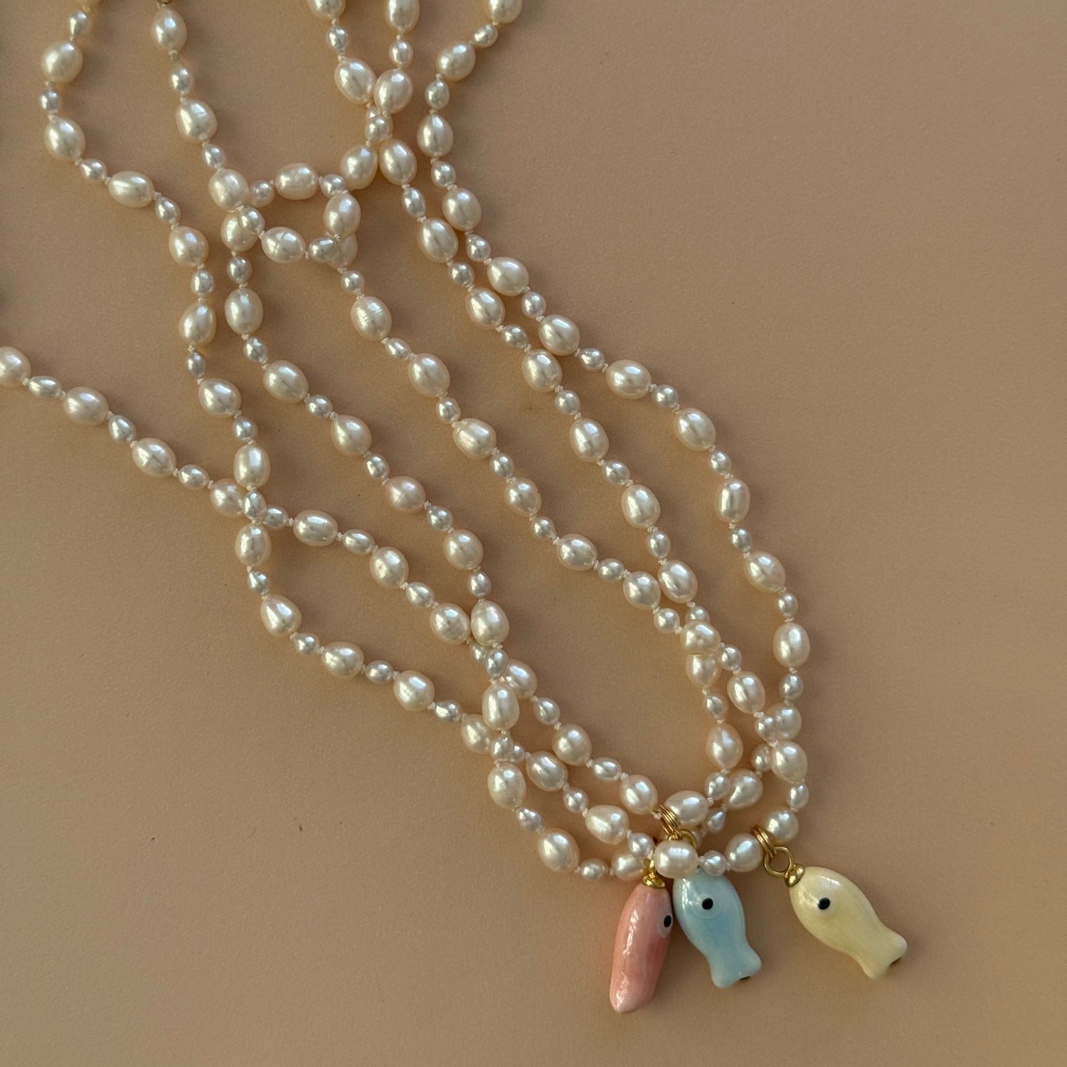 Pearl necklace with fish-shaped charms on a beige background