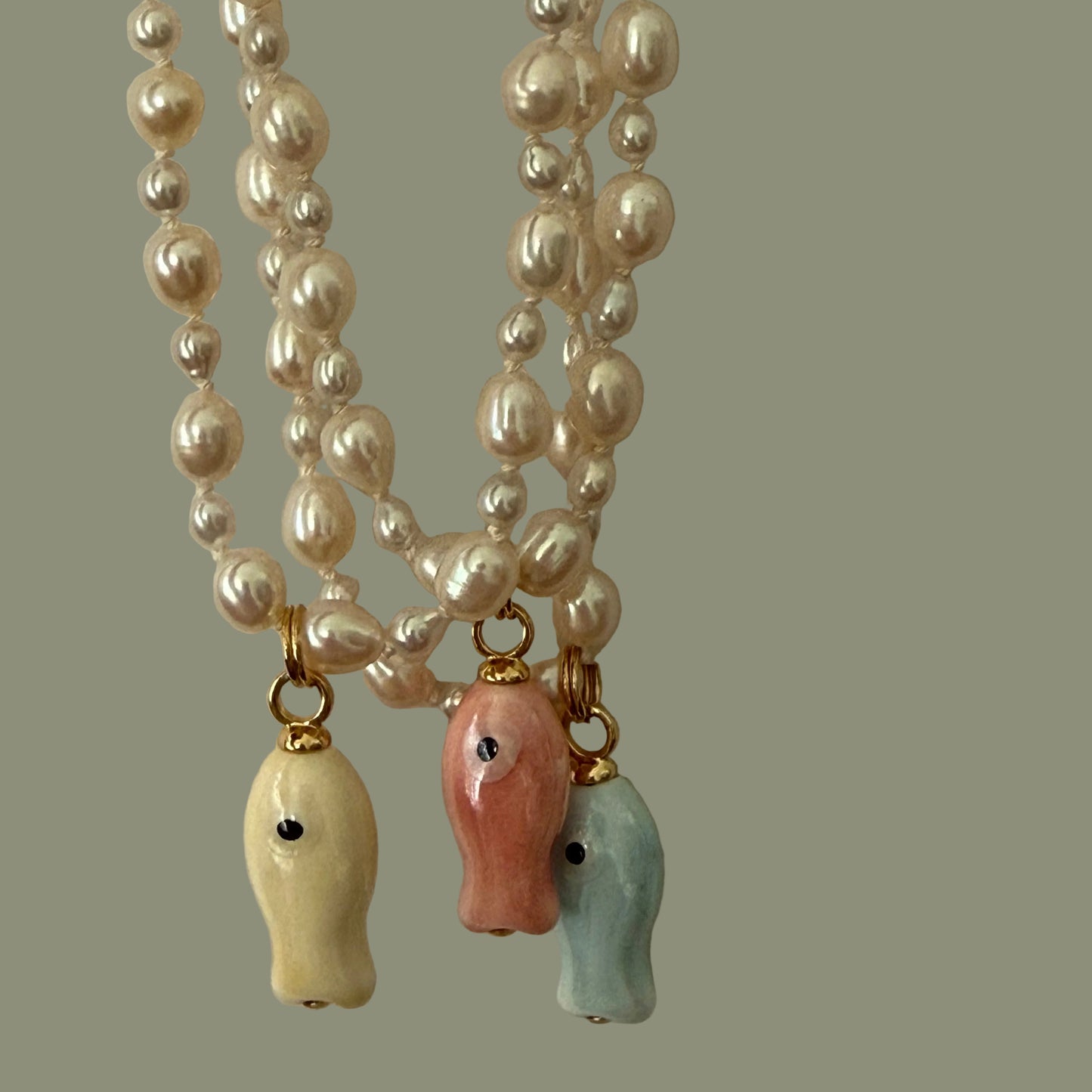 Pearl necklace with colorful ceramic fish pendants on a beige background