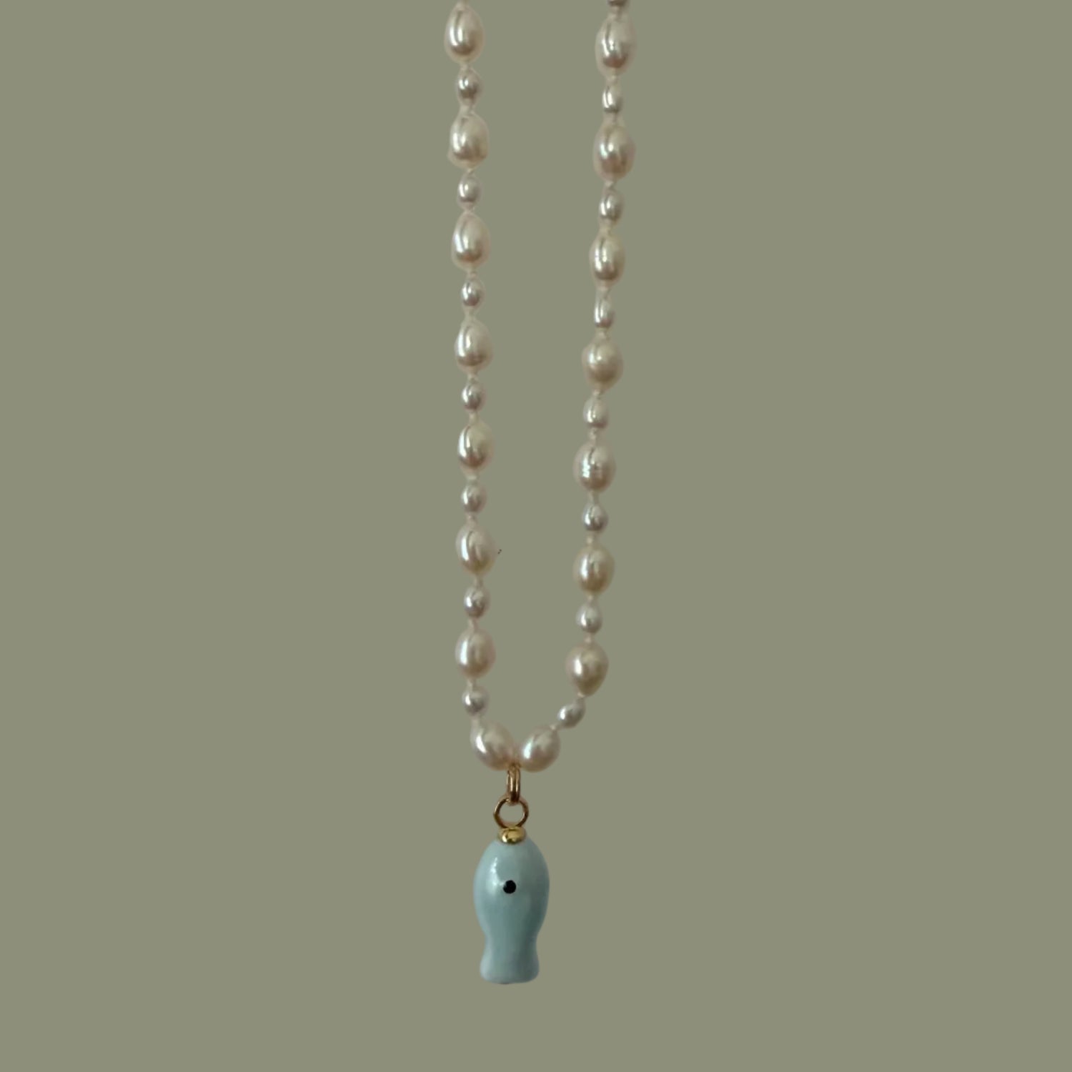 Pearl necklace with a blue fish pendant on a plain background