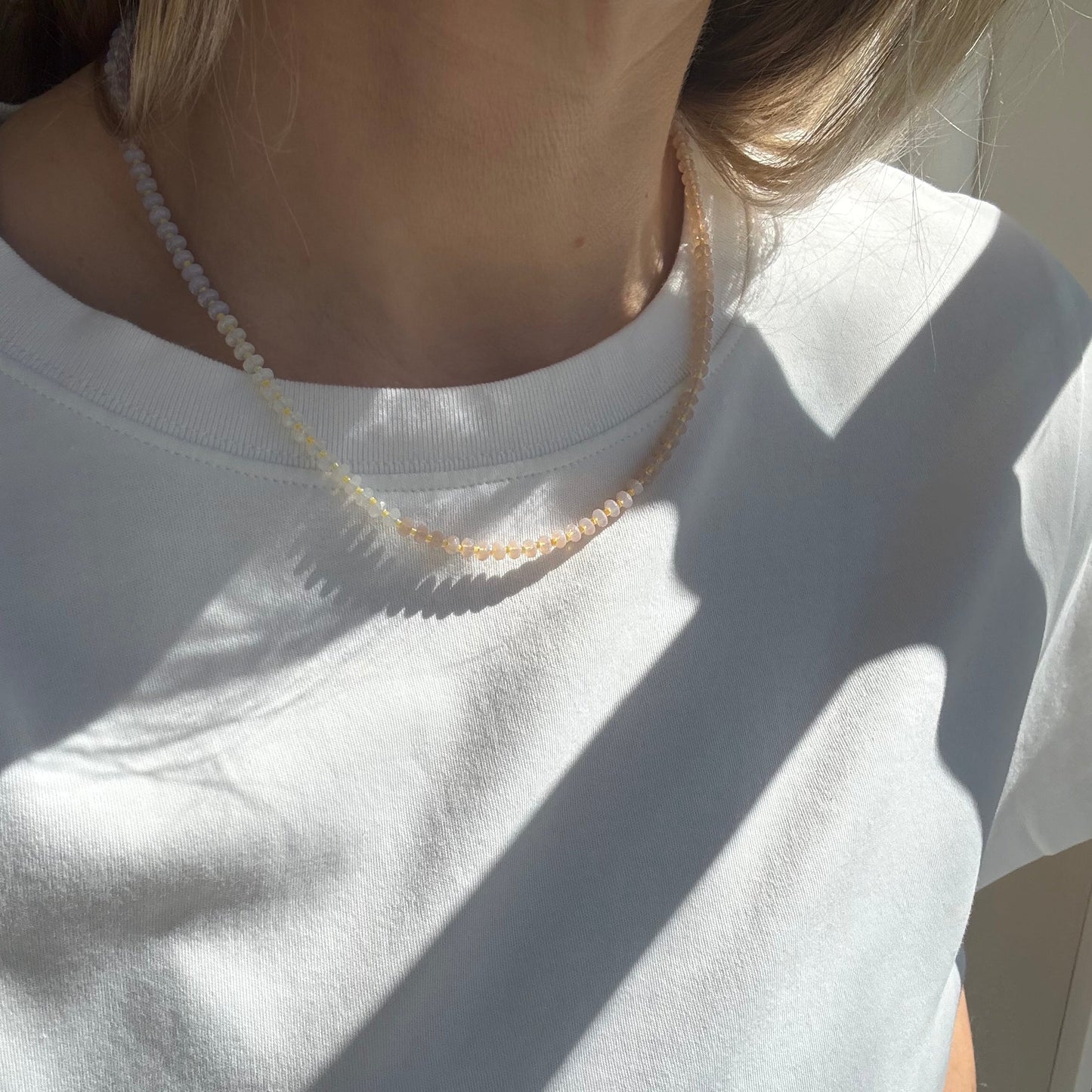 Person wearing a white shirt with a necklace, sitting on a white surface.