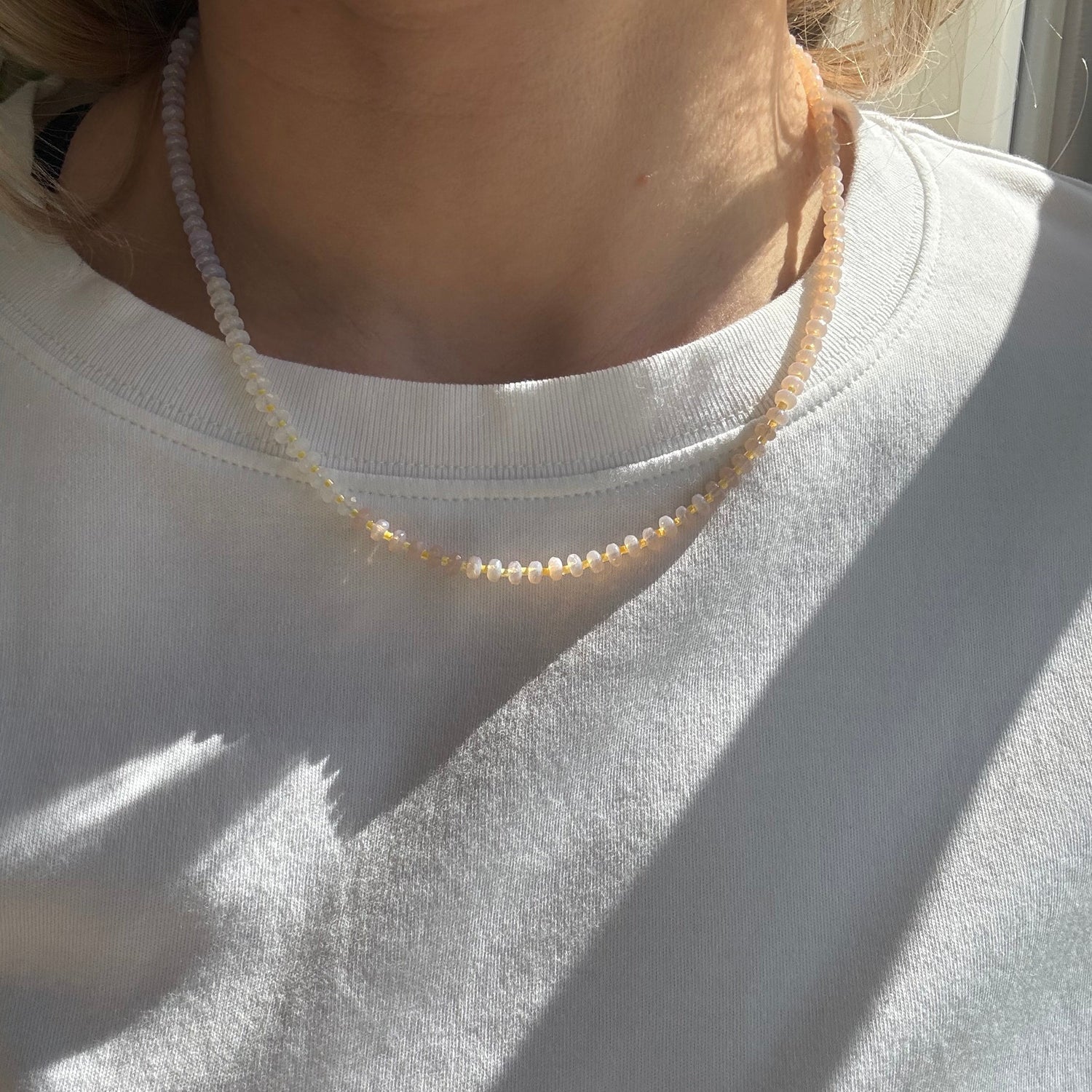 Close-up of a person wearing a beige sleeveless top with a white shirt underneath.