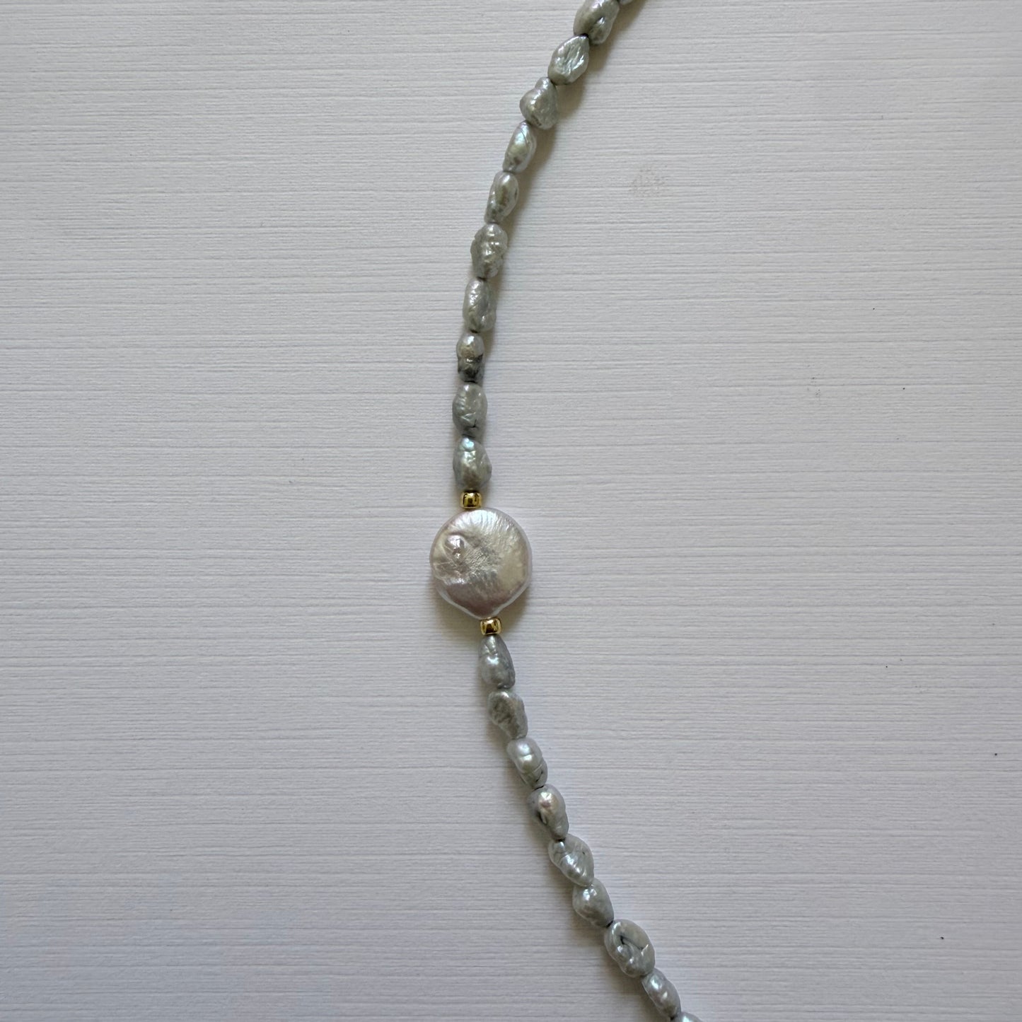 Silver chain necklace with a round freshwater coin pearl on a light gray background