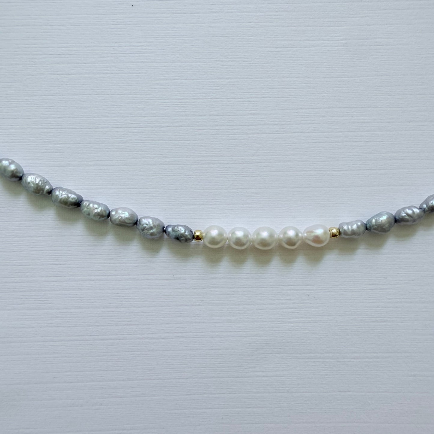Necklace with alternating blue gray and white pearls on a light gray background