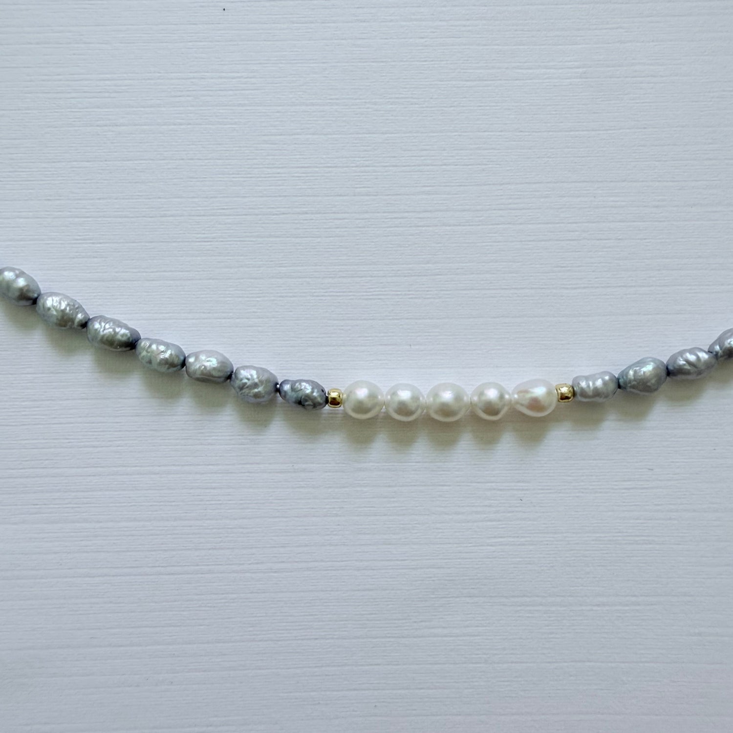 Necklace with alternating blue gray and white pearls on a light gray background