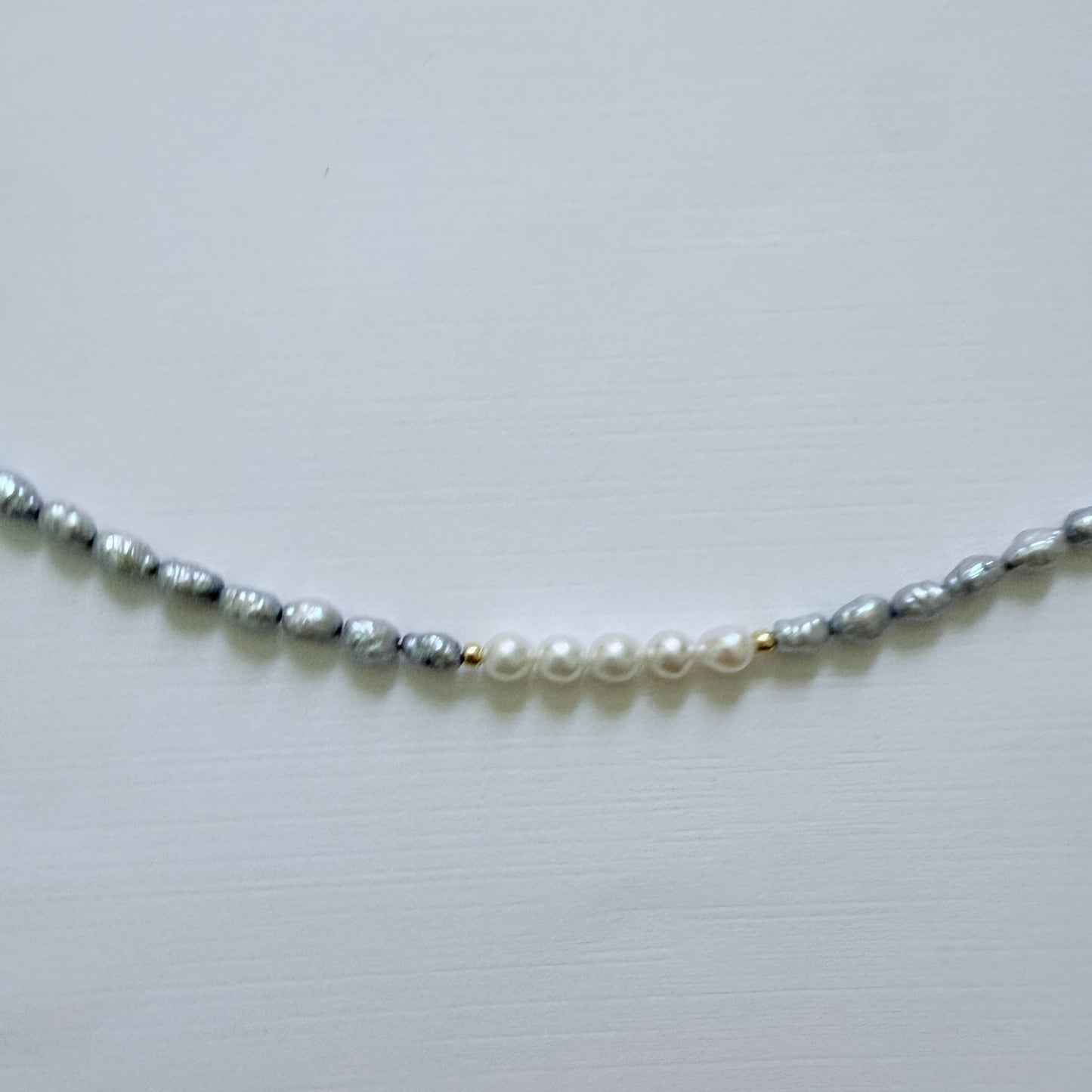 Necklace with alternating blue grey and white pearls on a light gray background