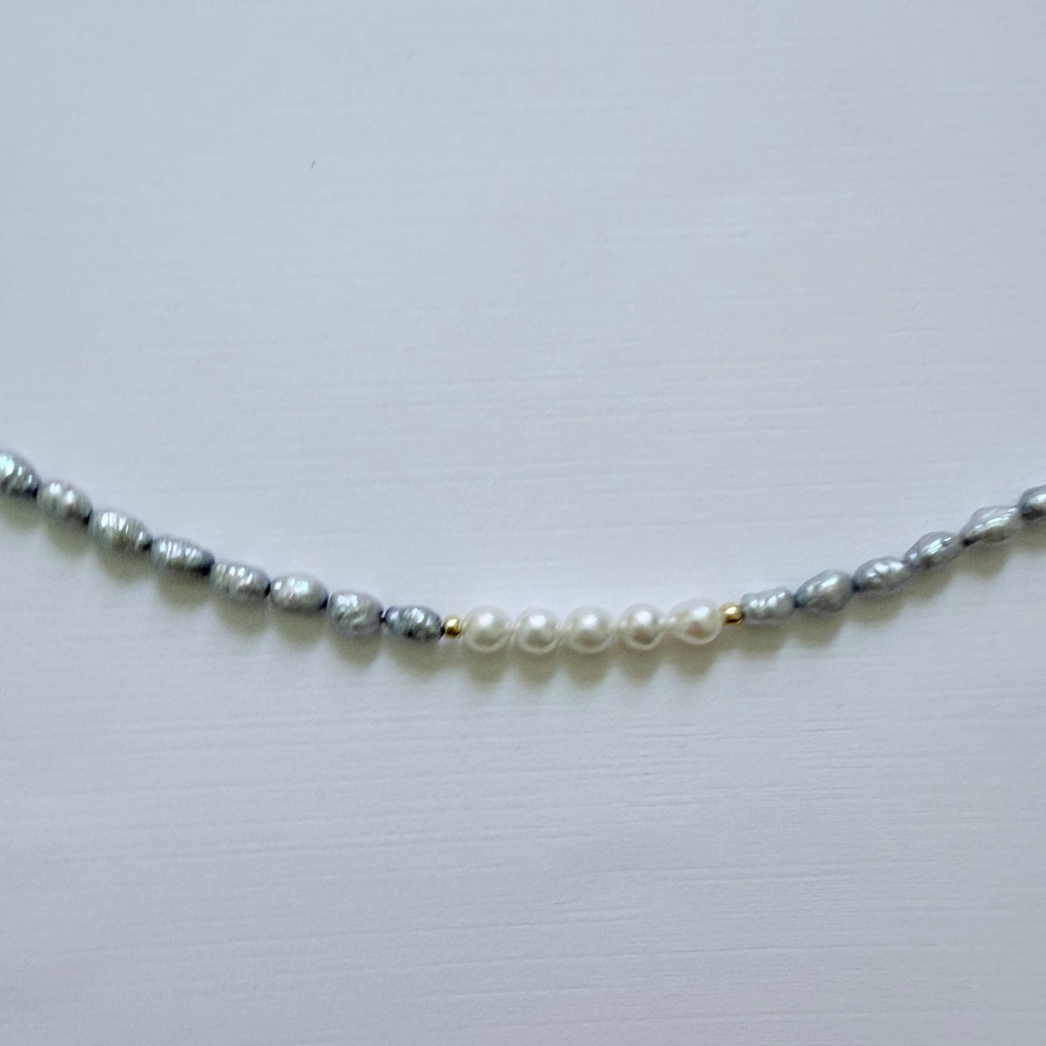 Necklace with alternating blue grey and white pearls on a light gray background