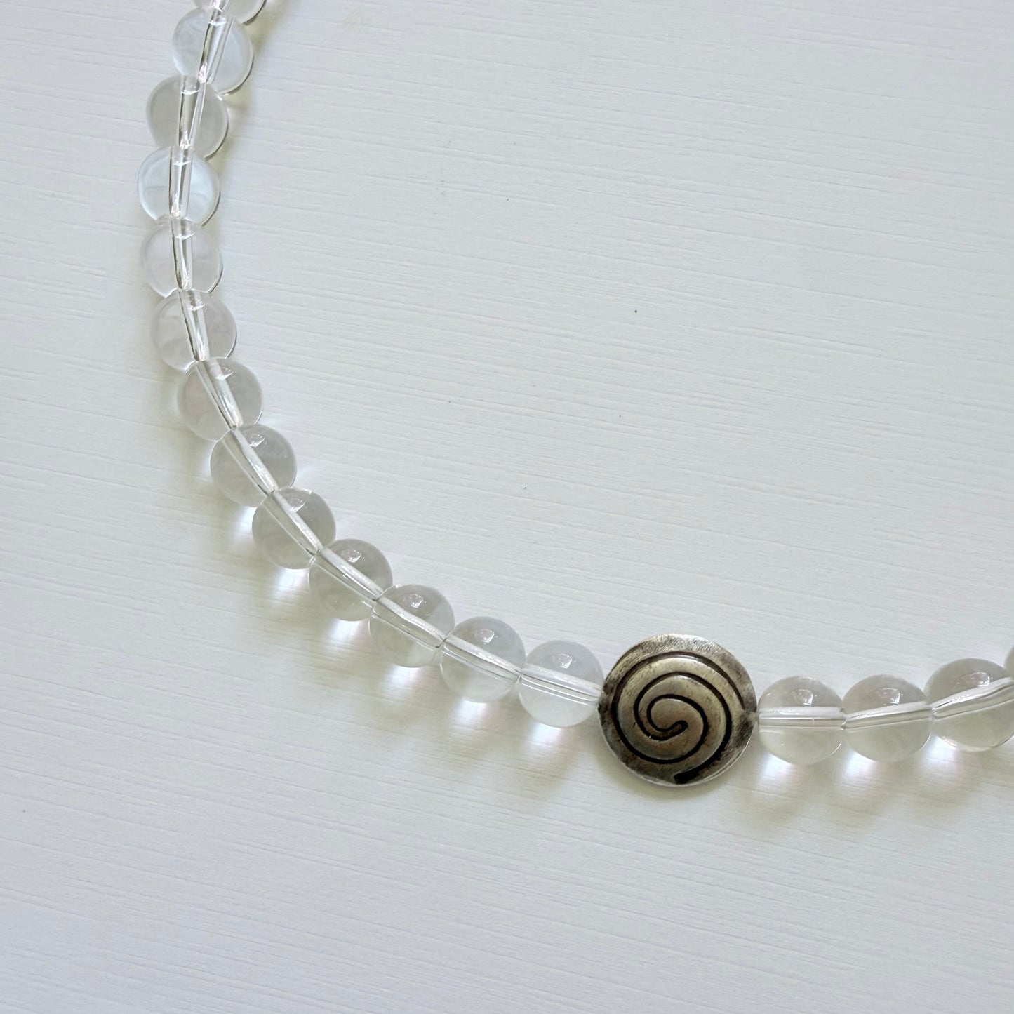 Necklace with clear beads and a black spiral pendant on a white background