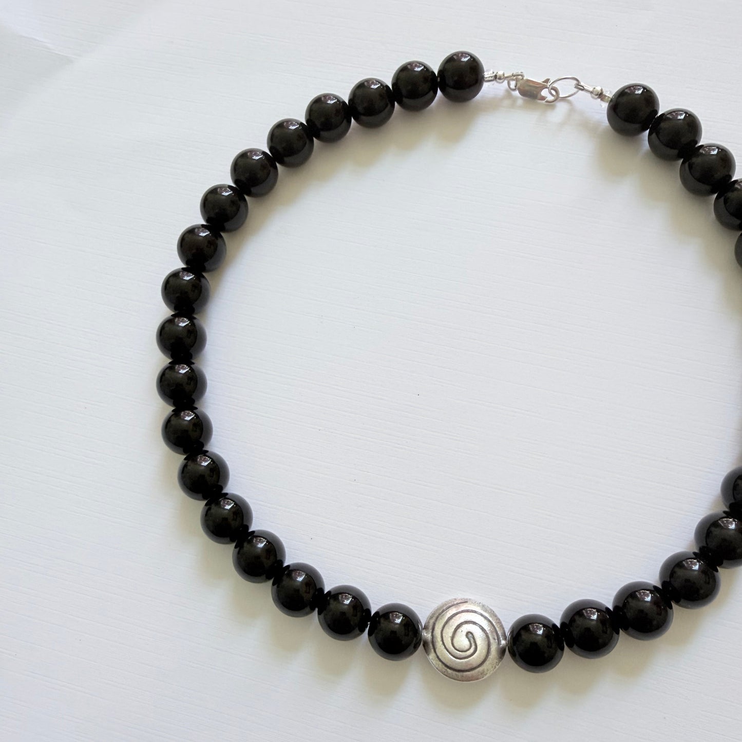 Black beaded necklace with a silver spiral pendant on a white background