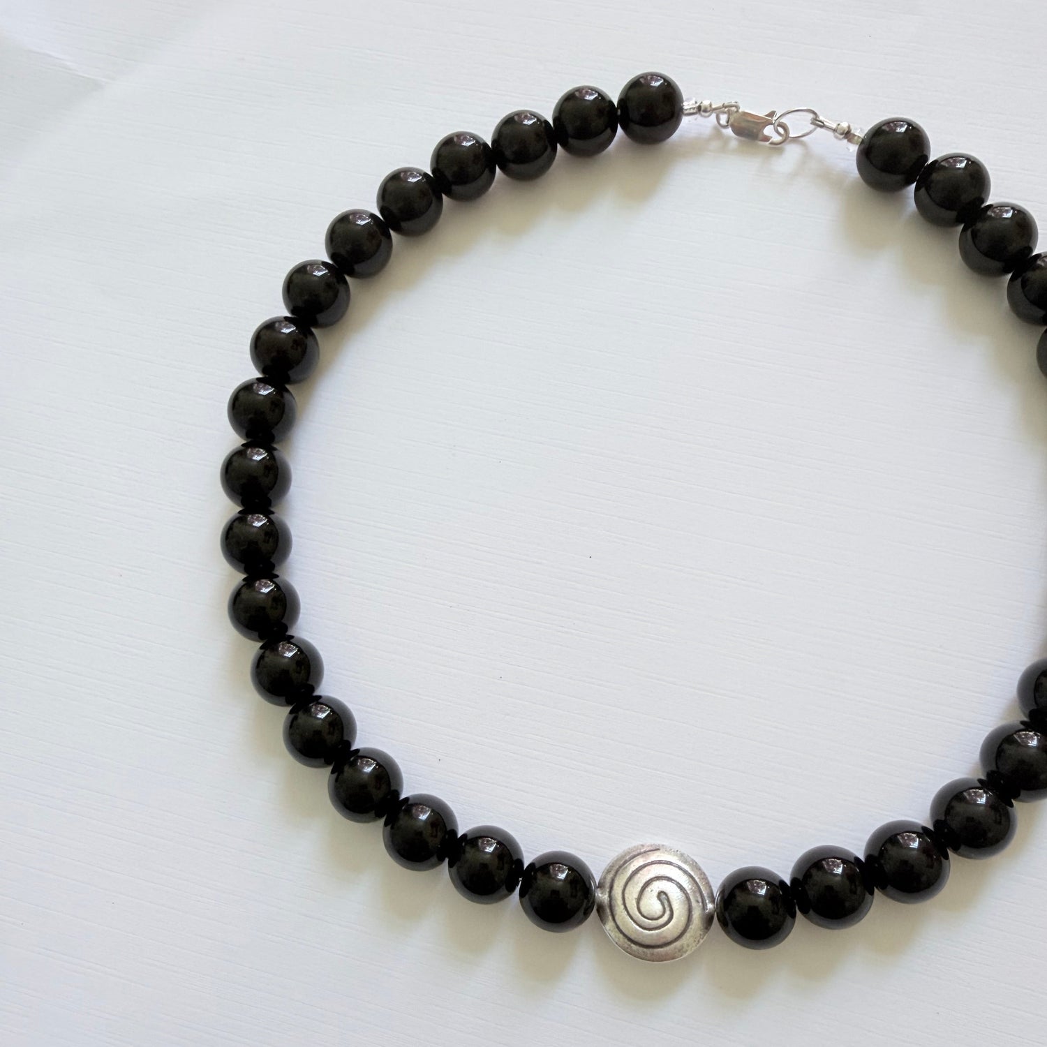 Black beaded necklace with a silver spiral pendant on a white background
