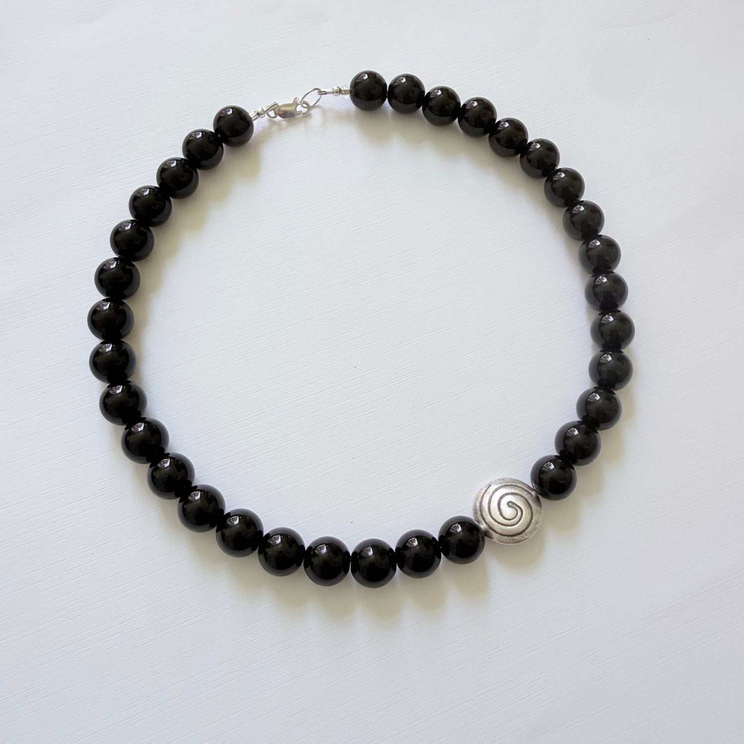 Black beaded nec with a silver spiral charm on a white backgroundlace