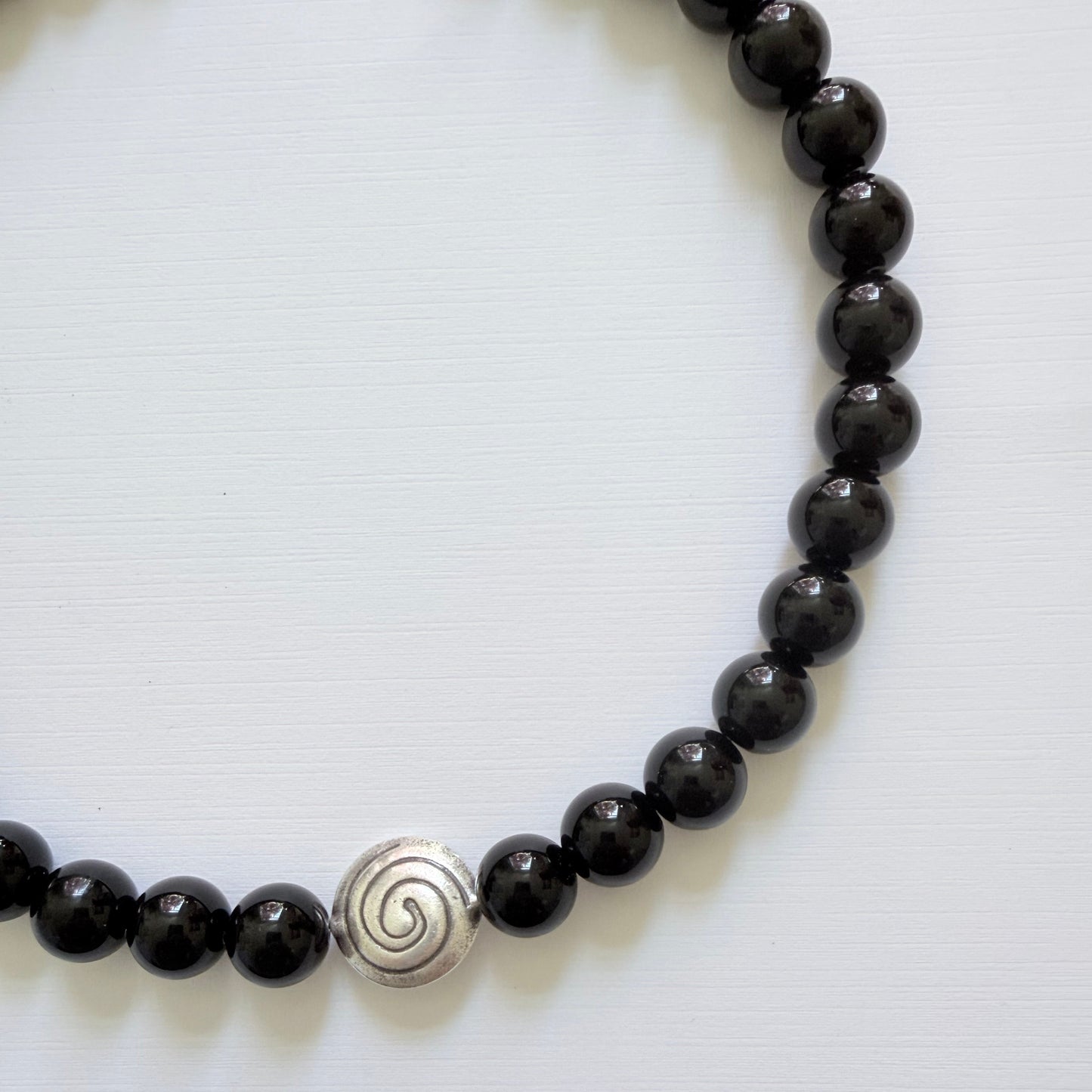 Black beaded bracelet with a silver spiral charm on a white background