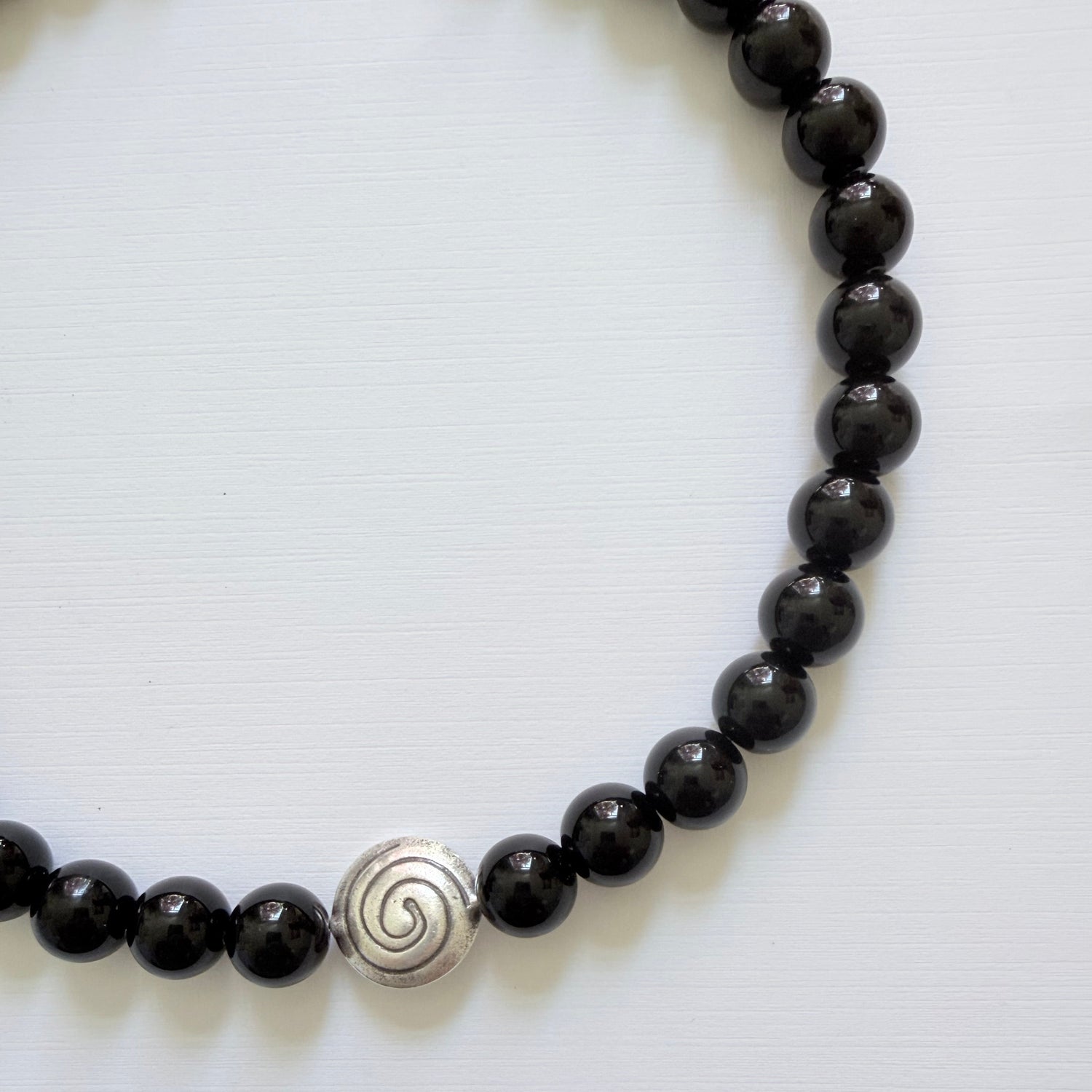 Black beaded bracelet with a silver spiral charm on a white background