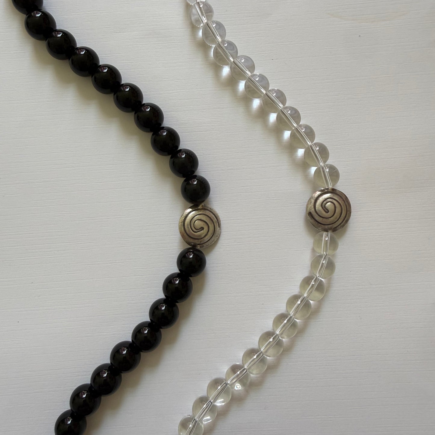 Two beaded necklaces, one clear and one black, on a white background.