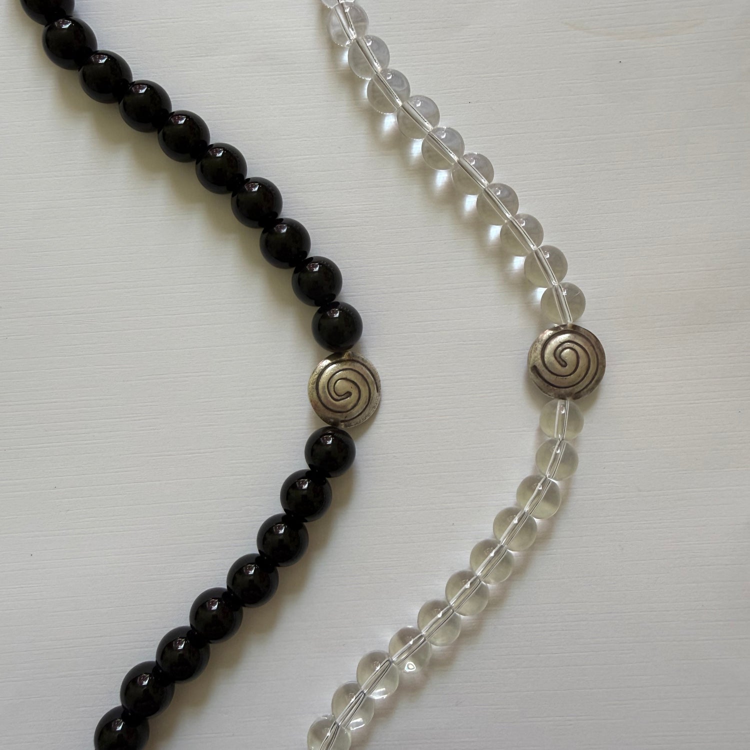 Two beaded necklaces, one clear and one black, on a white background.