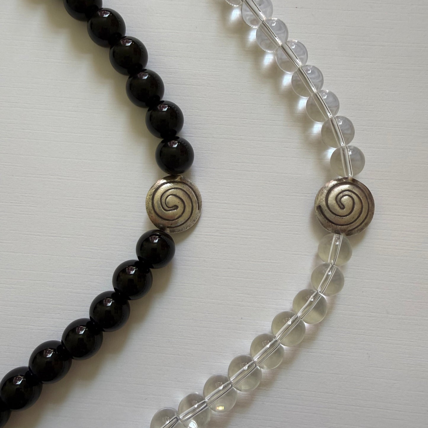 Two beaded necklaces, one clear and one black, with spiral clasps on a white background.