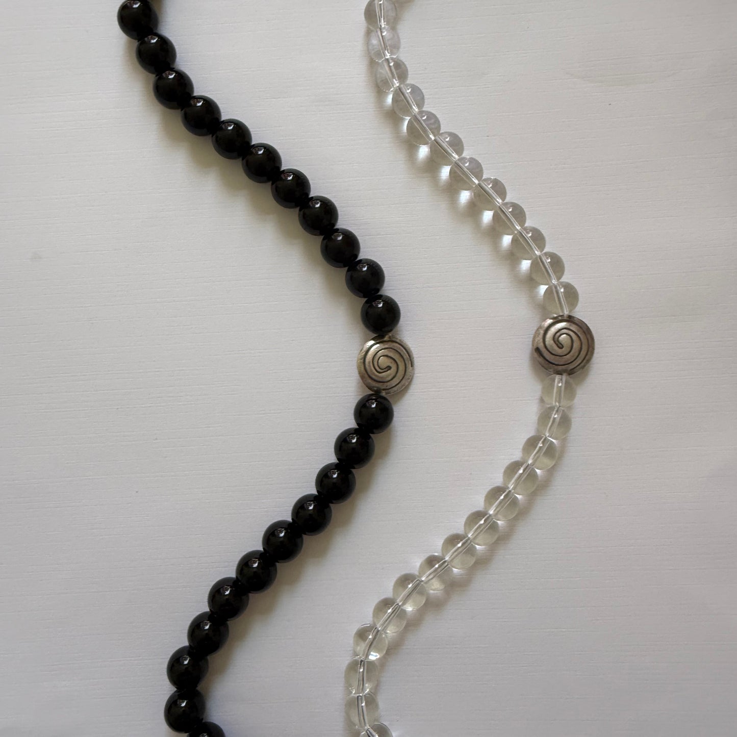 Two beaded necklaces, one black and one clear with silver clasps, on a white background.