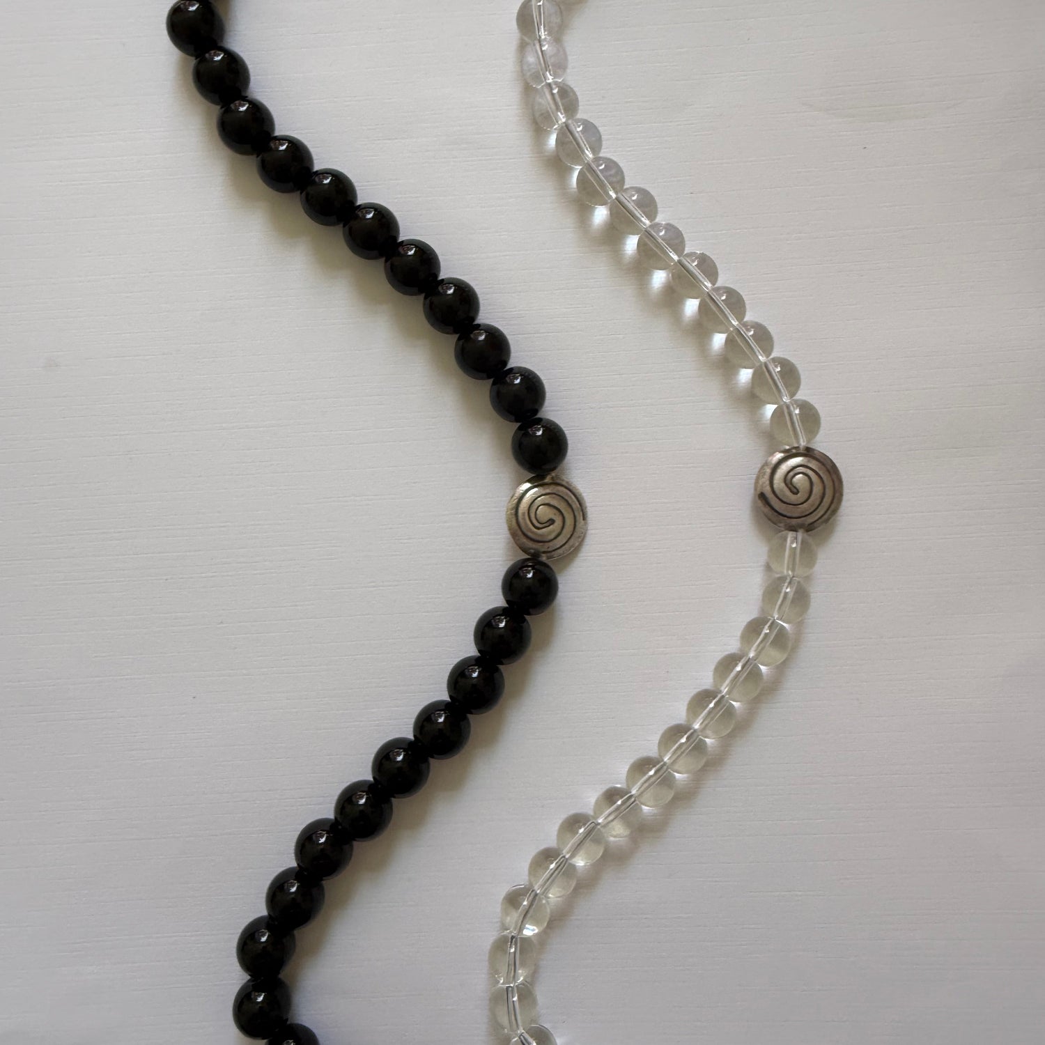 Two beaded necklaces, one black and one clear with silver clasps, on a white background.