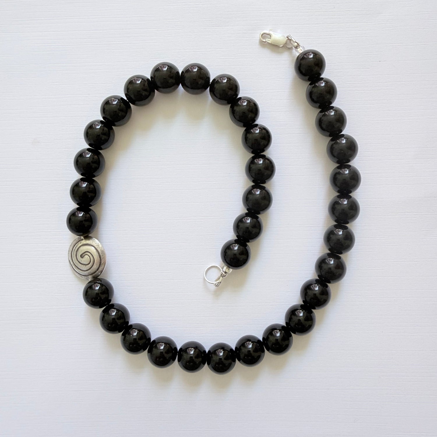 Black beaded necklace with a silver spiral pendant on a white background