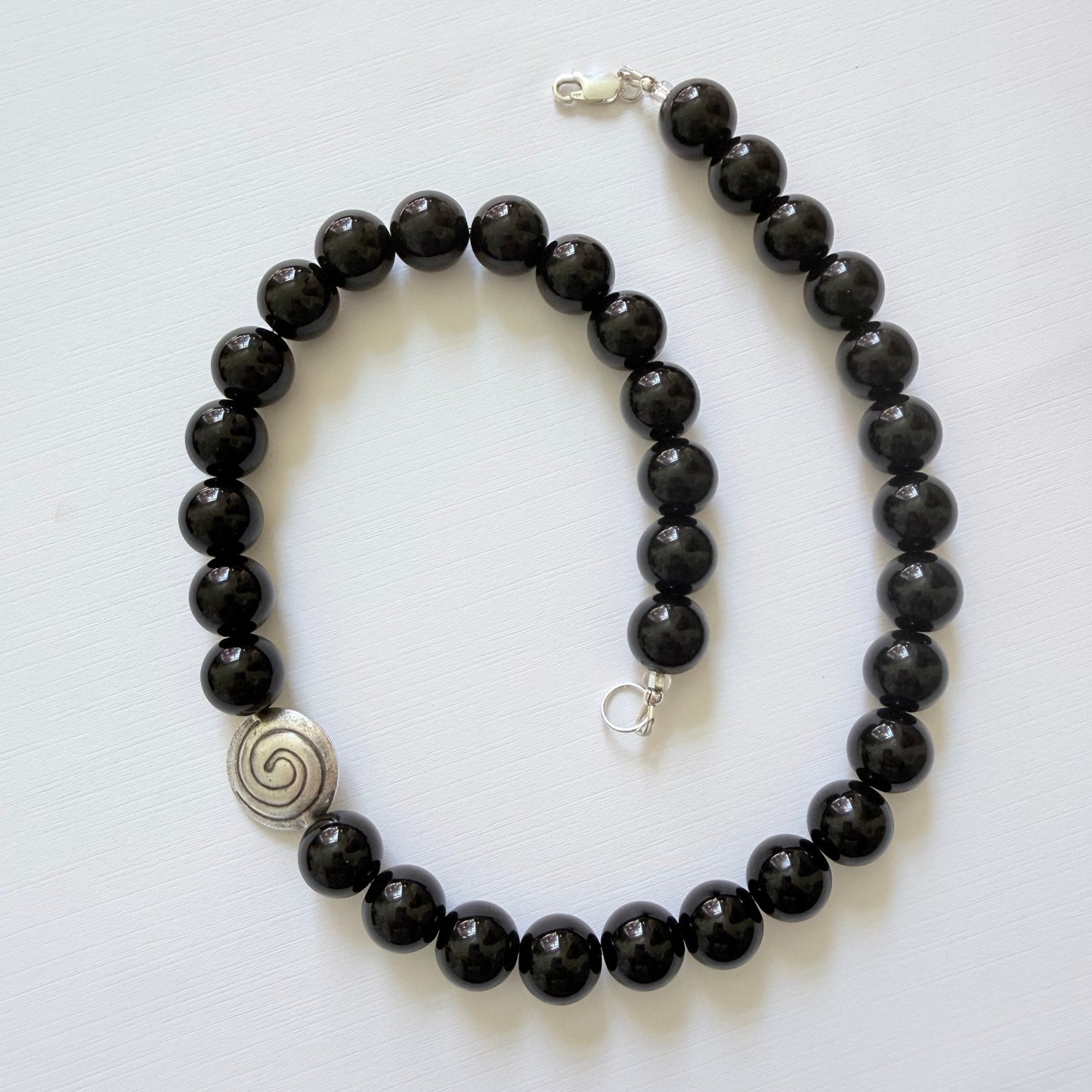 Black beaded necklace with silver clasp and spiral charm on a white background