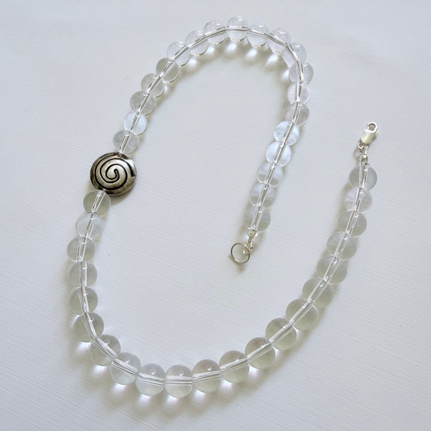 Clear beaded necklace with a spiral pendant on a white background