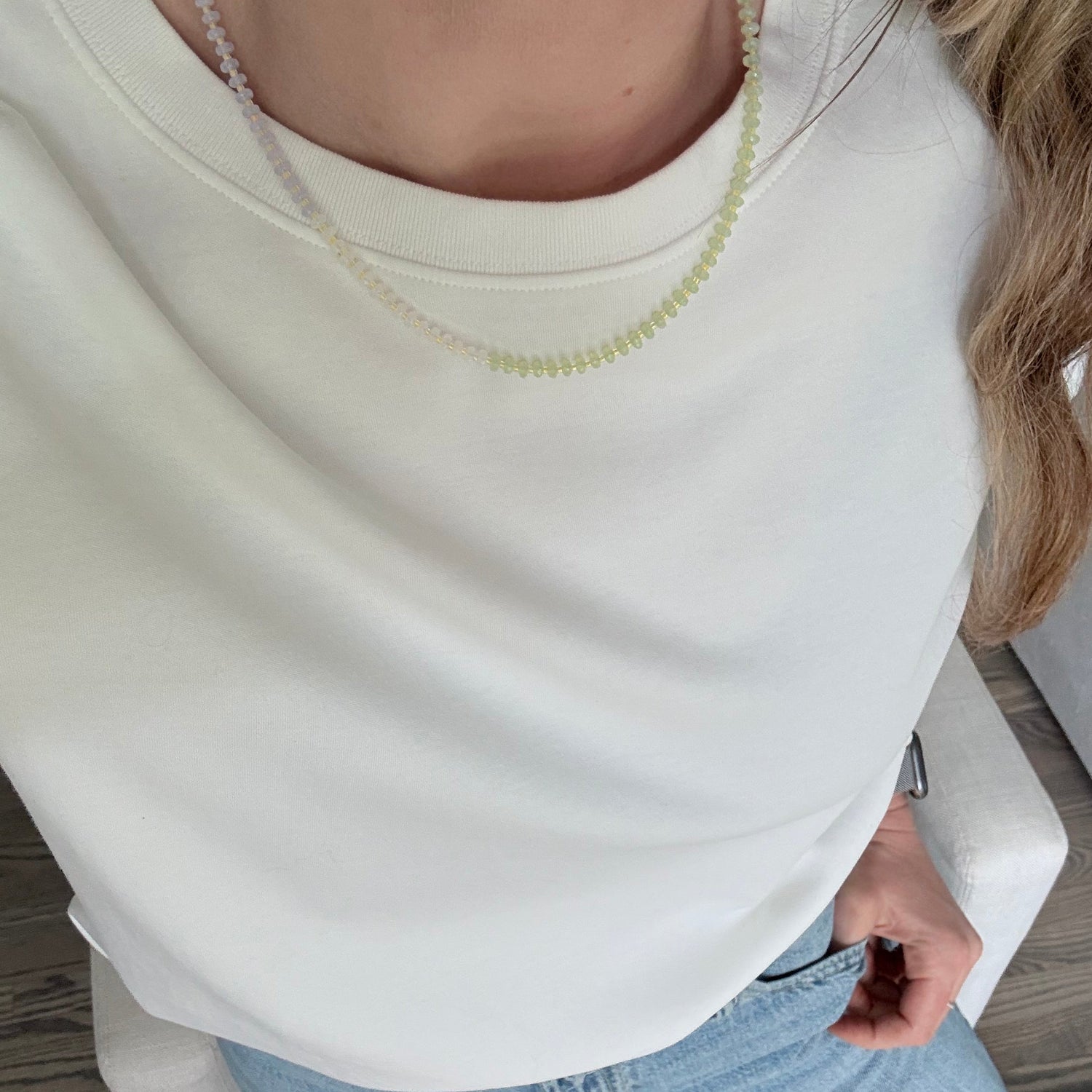 Person wearing a white top and light blue jeans sitting on a chair.