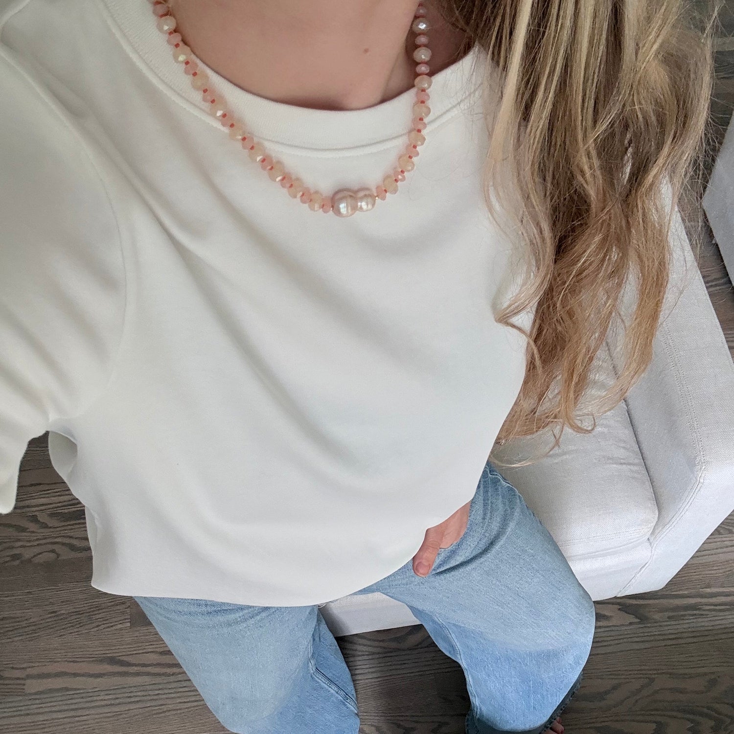 Person sitting on a wooden floor wearing a white shirt and blue jeans.