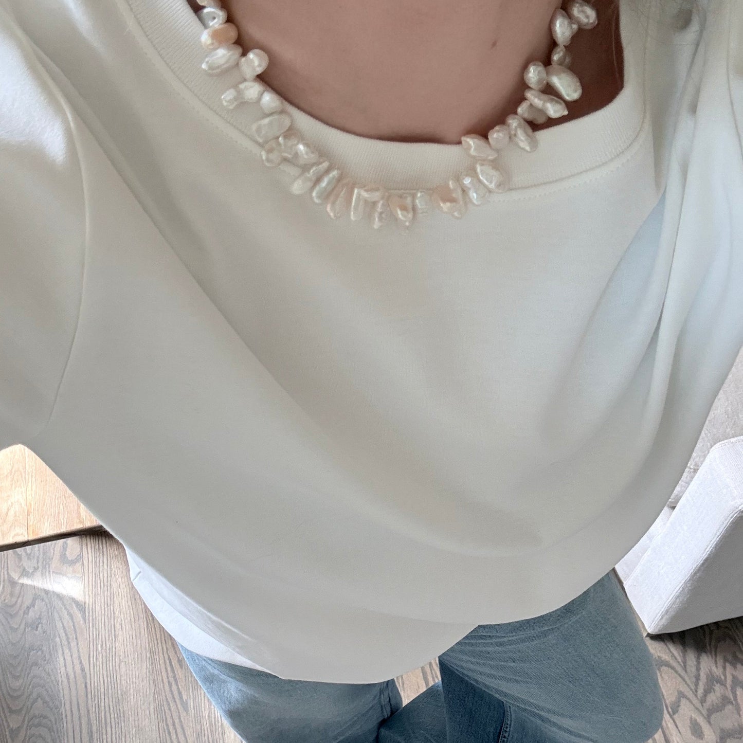 Person wearing a white dress with pearl details on a wooden floor.