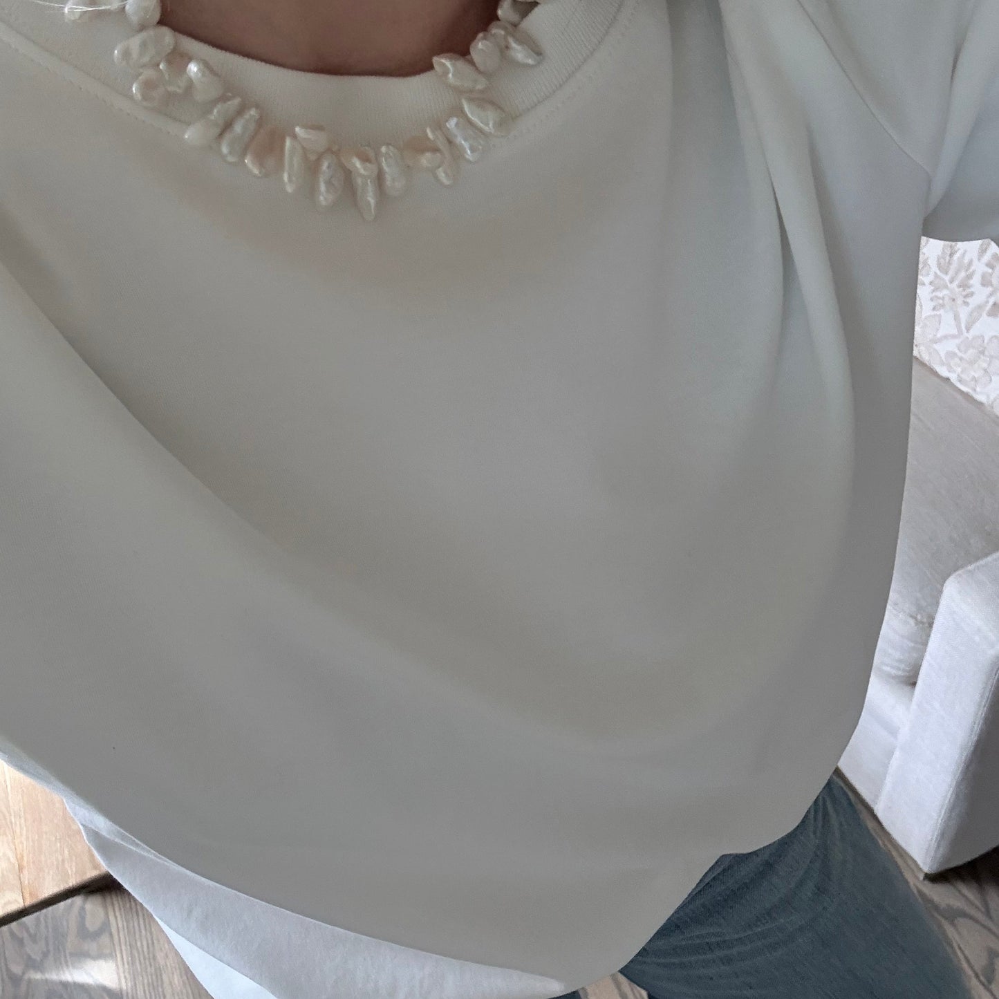 Close-up of a person wearing a white dress with pearl details on a wooden floor.