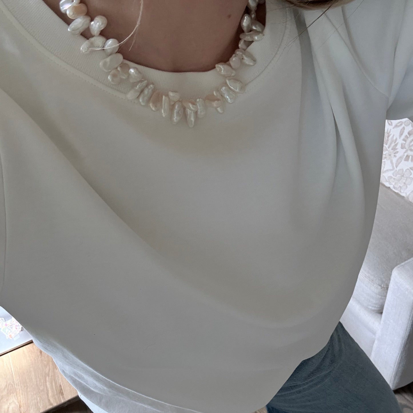 Close-up of a white dress with pearl details on a wooden floor.