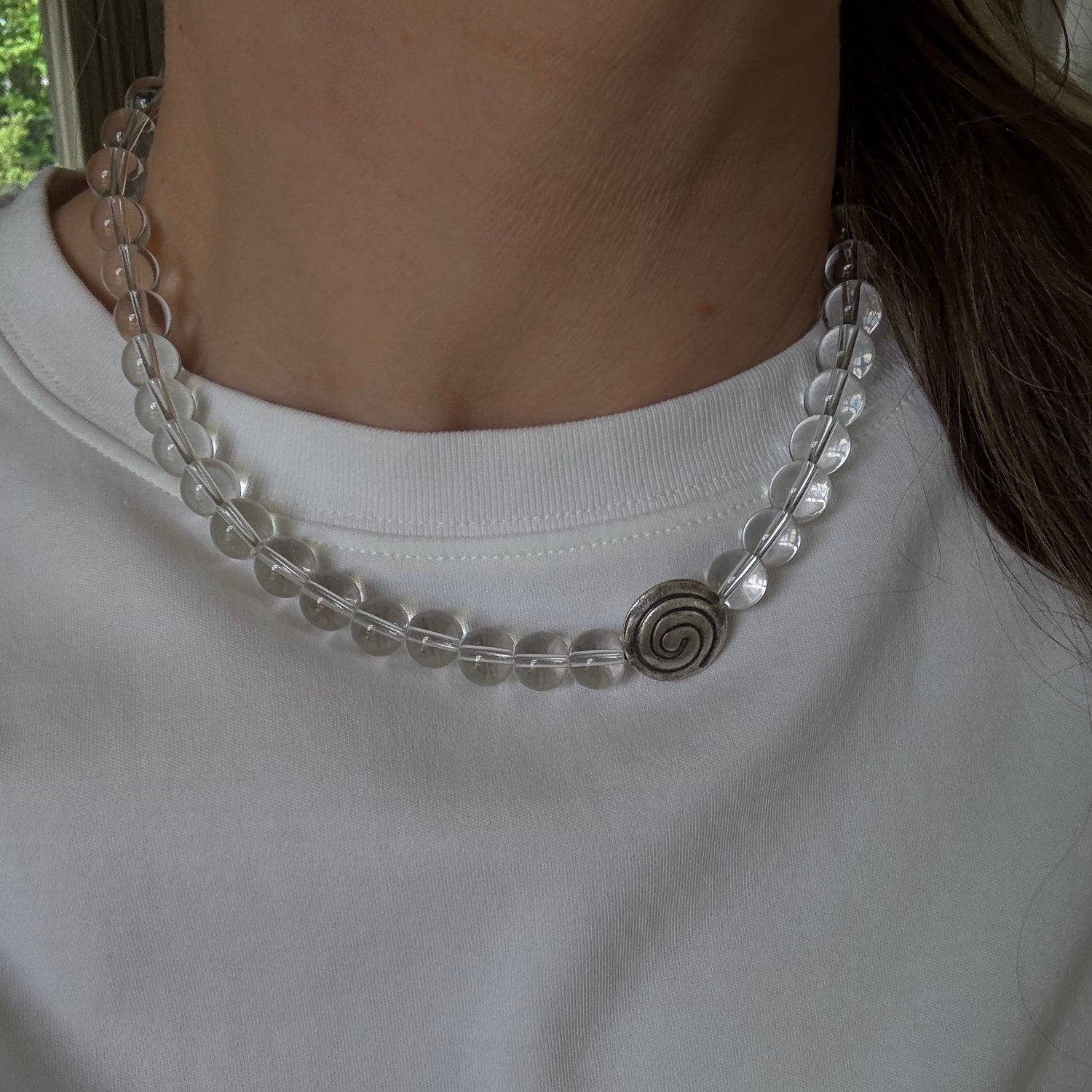 Close-up of a person wearing a clear beaded necklace with a white shirt.