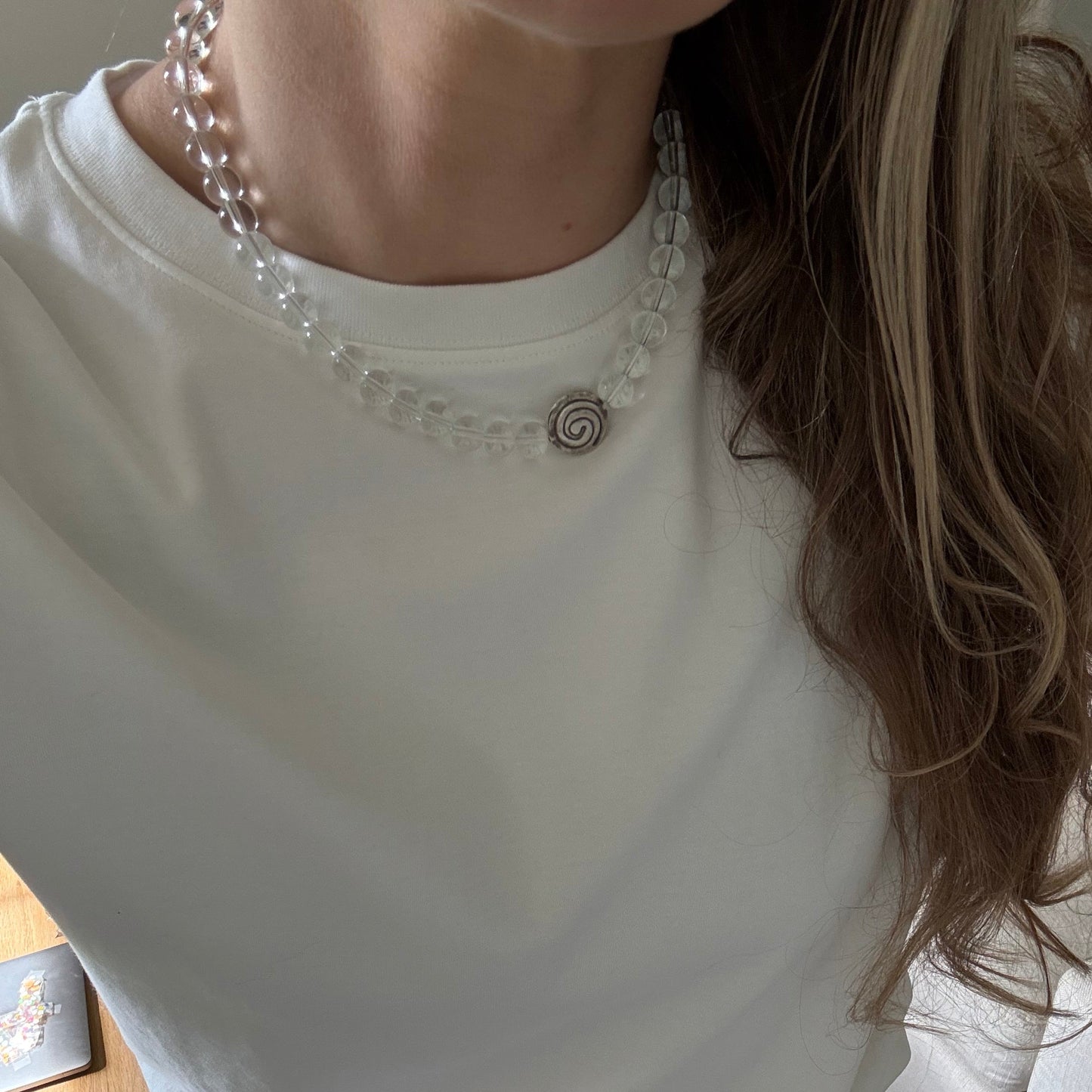 Person wearing a white top with decorative elements and blue jeans, sitting on a wooden floor.