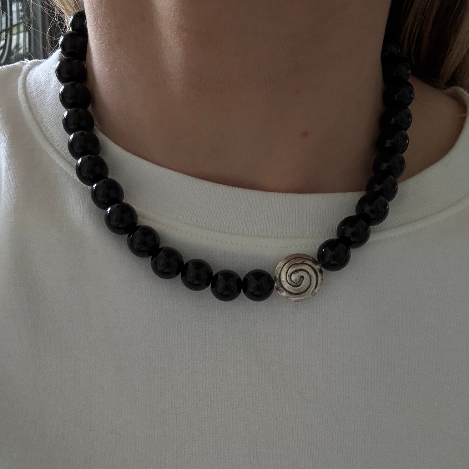 Black beaded necklace with a silver spiral pendant on a plain background