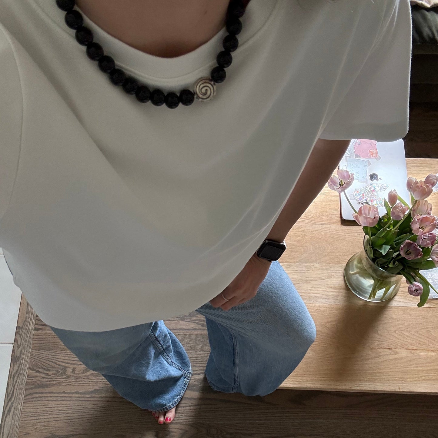 Person sitting on a white chair with a wooden floor and a vase of flowers in the background