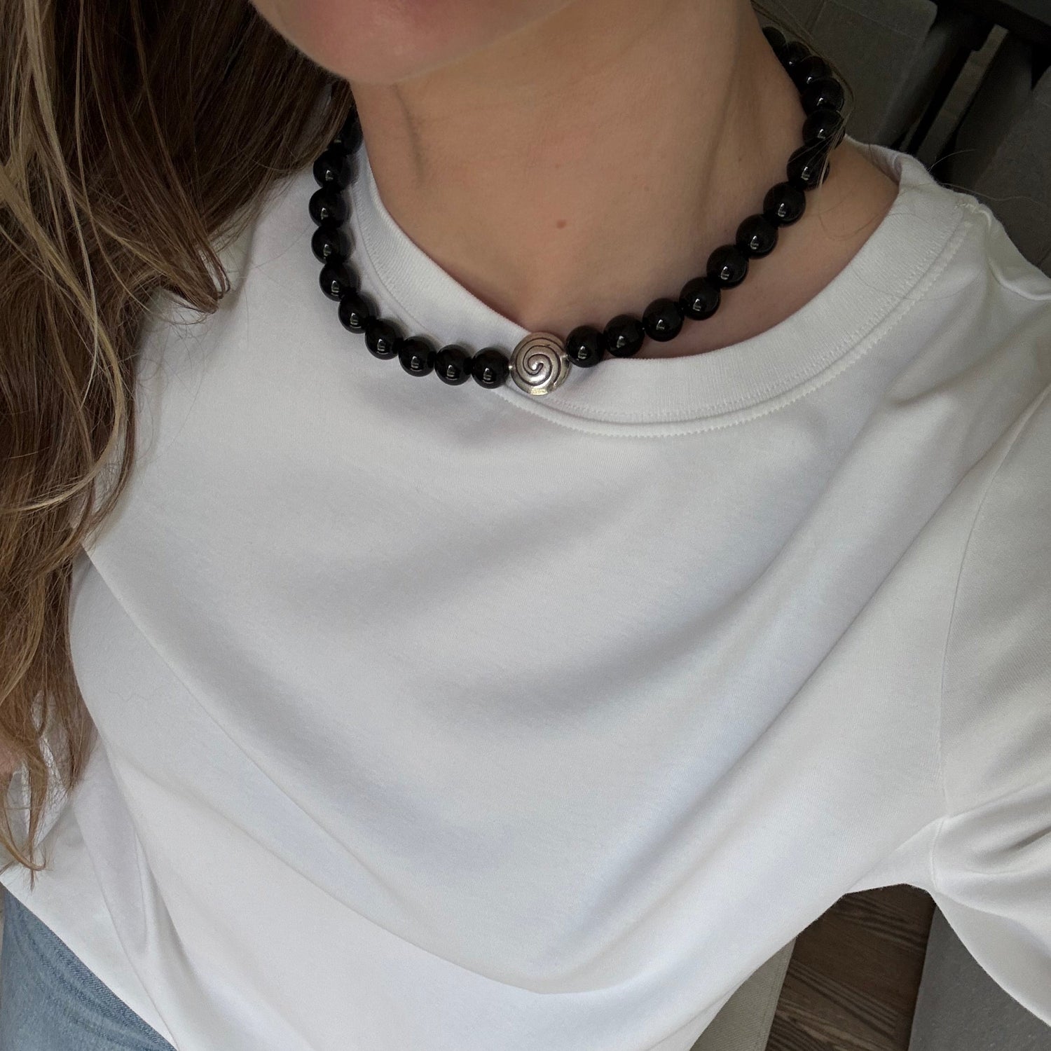 Person wearing a white shirt and blue jeans with a black beaded bracelet.