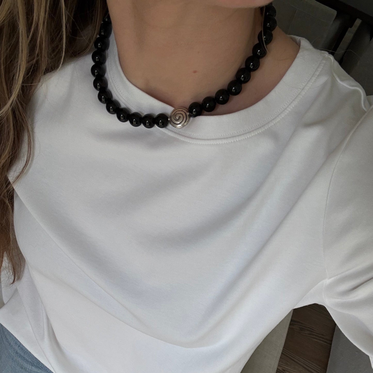 Person wearing a white shirt and blue jeans with a black beaded bracelet on a wooden floor.